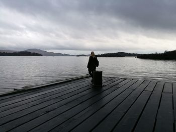 Rear view of woman standing by lake on jetty