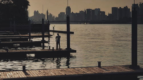 Pier on river by city buildings against sky