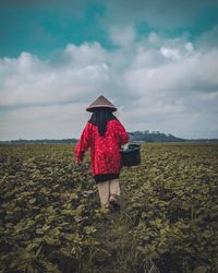 Rear view of woman with bucket on field against sky