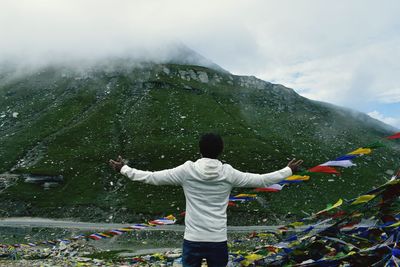 Rear view of man standing by prayer flags and mountain against sky