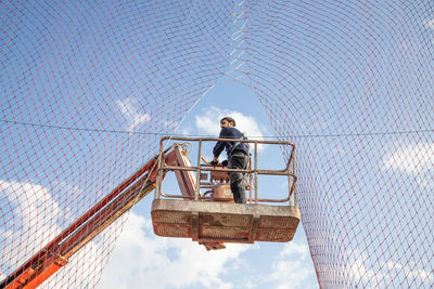 Low angle view of man working while standing on crane