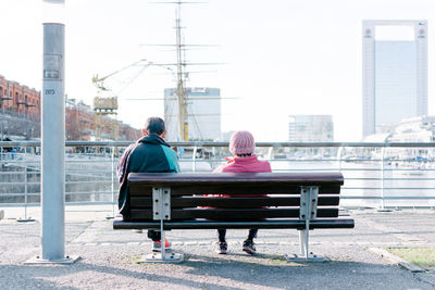 Rear view of people sitting on bench against sea