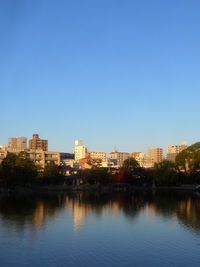 Buildings by river against clear blue sky