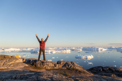 Rear view of woman standing on rock against sky