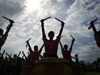 Silhouette girls at parade while banging drums against sky