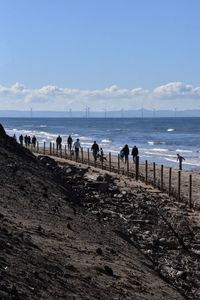 People on shore at beach against sky