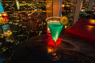 Close-up of martini glass on table against illuminated cityscape