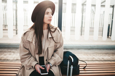 Sad traveler woman in hat sitting on a public transport stop
