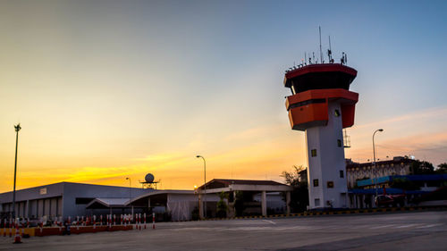 Lighthouse by building against sky during sunset