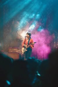 Woman singing in microphone while playing guitar at music concert