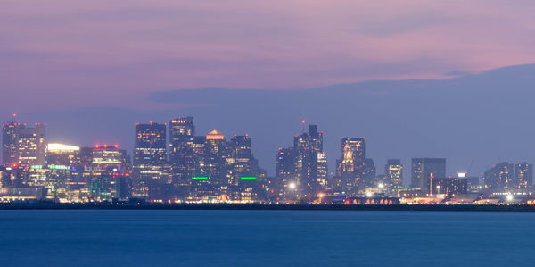 Illuminated city by sea against sky at night