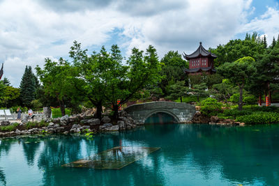 Arch bridge over river amidst trees and buildings against sky