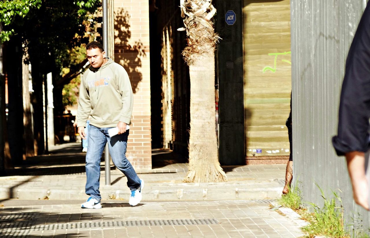 rear view, lifestyles, built structure, full length, architecture, building exterior, walking, casual clothing, tree, standing, men, leisure activity, the way forward, person, day, sunlight, outdoors