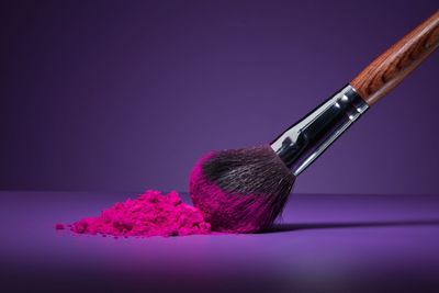Close-up of make-up brush and pink face powder on purple table