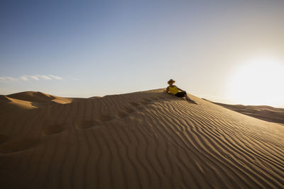 Senior woman relaxing at desert against clear sky during sunny day