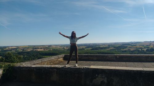 Full length of carefree woman standing on retaining wall against sky