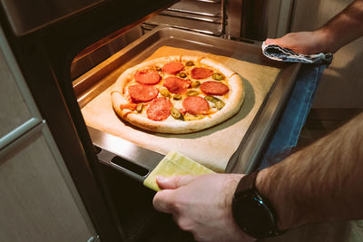 A man pulls a tray of pepperoni pizza from the oven at home