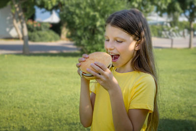 Funny teen girl with a burger in her hands on the background of the park.