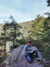 Young woman sitting on tree against sky