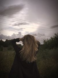 Rear view of woman with hands in hair standing on land