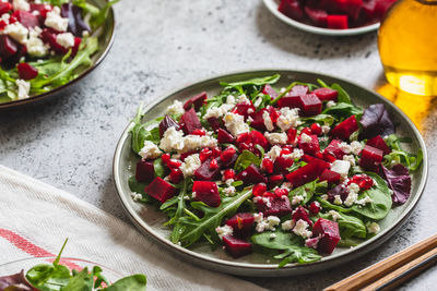 Arugula, beet and cheese salad with pomegranate and dressing on plate on grey stone kitchen table 