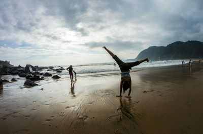 Woman doing handstand at beach against sky