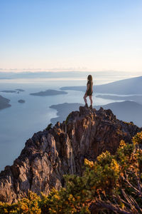 Man standing on rock looking at mountain against sky