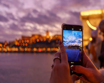 Low section of person photographing through smart phone against sky