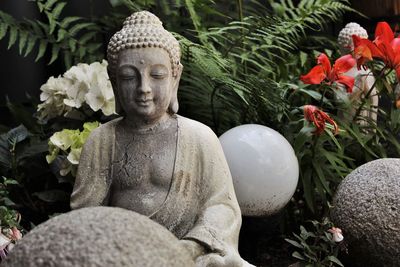 Statue of buddha against plants and stone wall