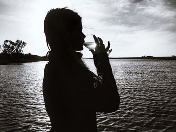 Rear view of silhouette woman standing by lake against sky