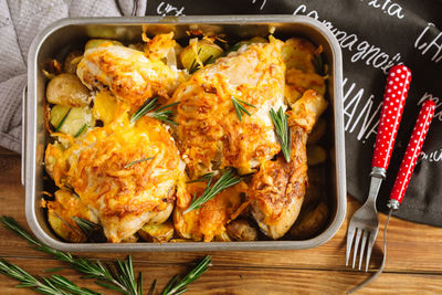 Chicken thighs baked with cheese on potato wedges and rosemary. iron baking dish.