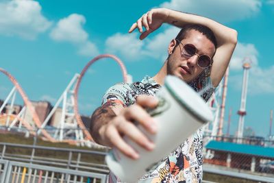 Midsection of young man holding sunglasses against sky in city