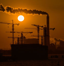 Factory emitting smoke against sky during sunset