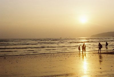 Silhouette people on beach against sky during sunset