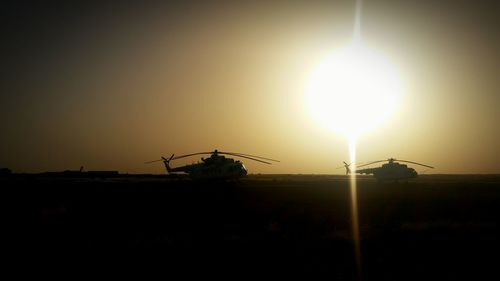 Silhouette of wind turbines on field against sky at sunset