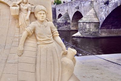 Sand statue on river in front of historical bridge