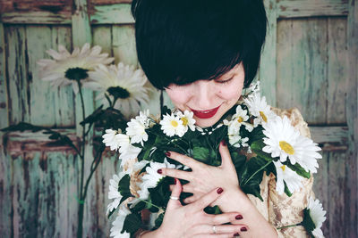 Close-up of smiling woman embracing flowers