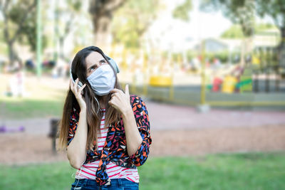 Woman wearing mask and headphones sitting at park