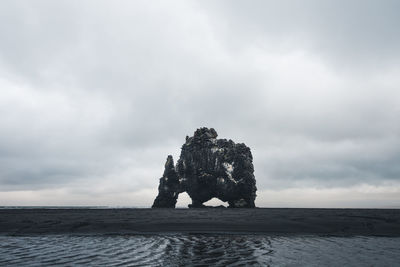 Sculpture in sea against cloudy sky