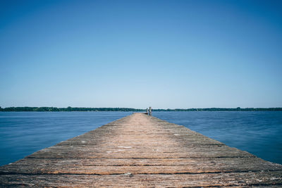 Pier over sea against clear blue sky