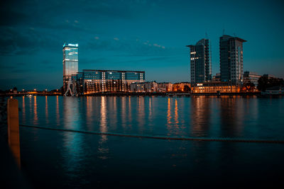 Illuminated buildings by sea against sky at night