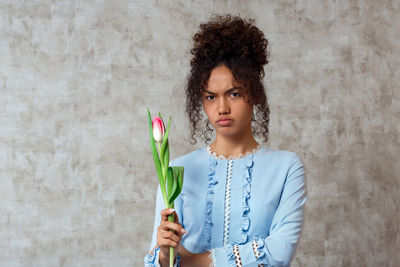 Portrait of young woman holding tulip while standing against wall