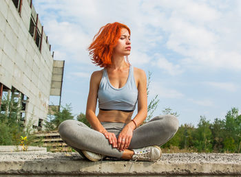 Full length of redhead young woman sitting on retaining wall