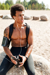 Shirtless young man looking away while relaxing on beach