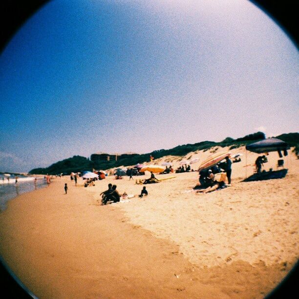 beach, sand, sea, transportation, clear sky, shore, large group of people, mode of transport, vacations, mountain, leisure activity, sky, copy space, men, lifestyles, travel, scenics, nature, tranquil scene