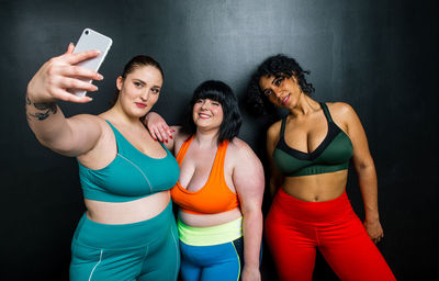 Smiling women taking selfie standing against wall