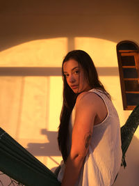 Young woman looking away while standing against sunset