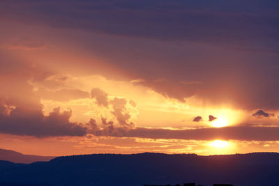 Scenic view of dramatic sky over silhouette landscape during sunset