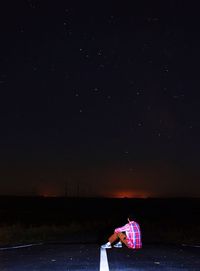 Man sitting on road while looking at stars against sky