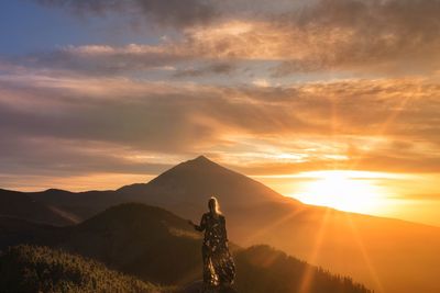 Rear view of woman standing on mountain against sky during sunset